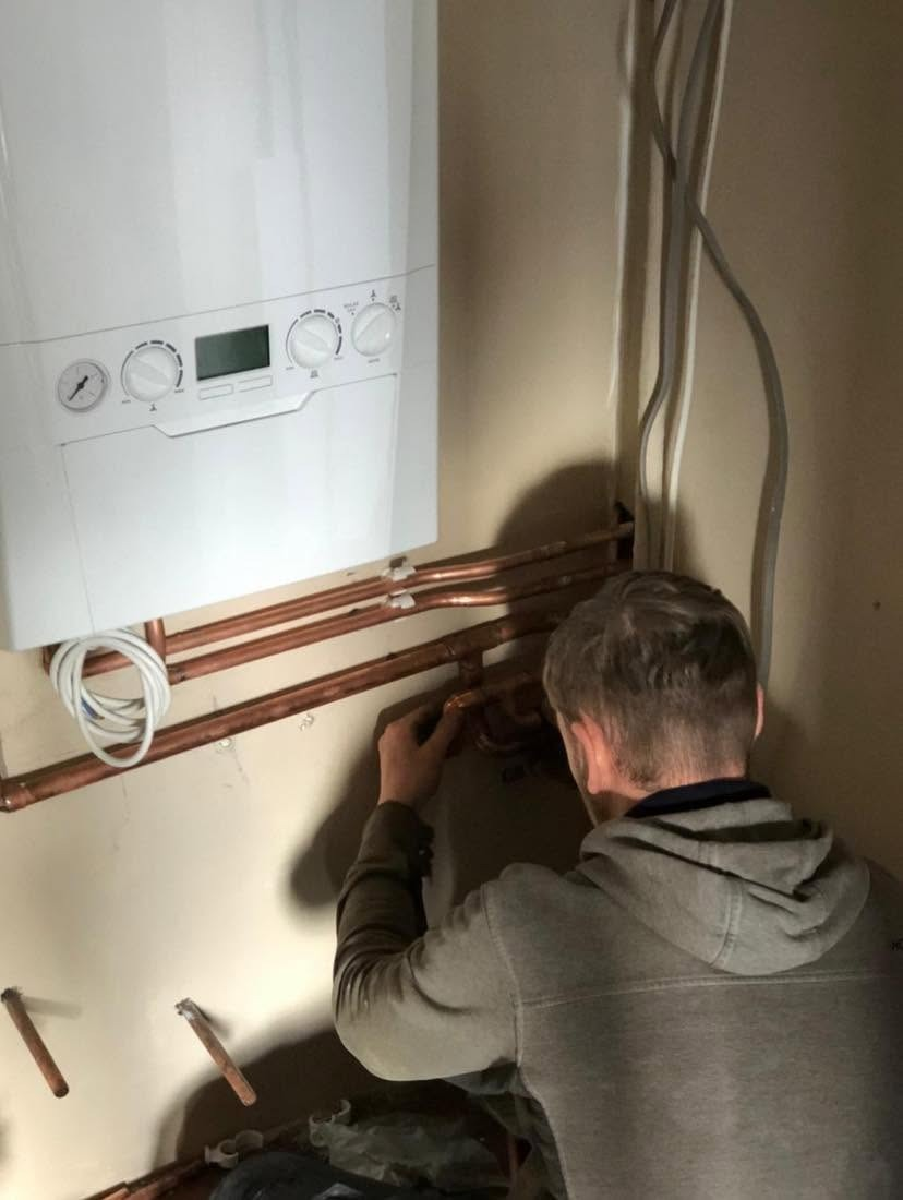 Gas Safe registered engineer connecting copper pipework beneath a newly fitted wall-hung gas boiler