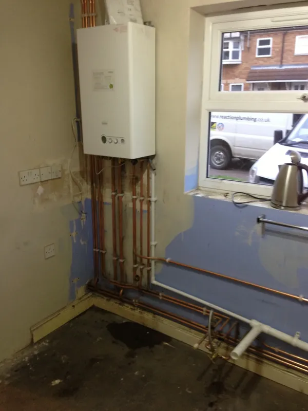 New build heating installation with a boiler and vertical copper flow and return pipework on a freshly plastered wall